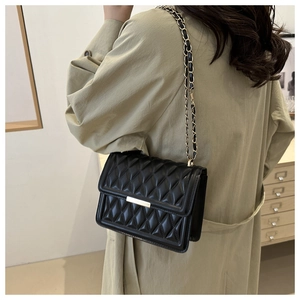 Close-up of black quilted crossbody bag with gold buckle and chain strap on model