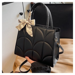 Detail of black quilted leather handbag featuring a silk scarf wrap and metal hardware