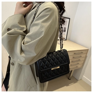Classic black quilted crossbody bag with gold metal trim worn by model in trench coat