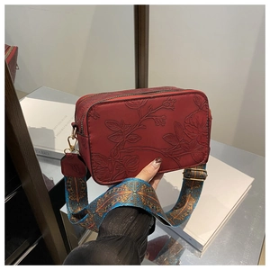 Detail of dark red leather shoulder bag with floral embossing and ethnic style wide strap