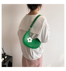 Detailed view of a green crescent bag with a white flower charm and adjustable strap