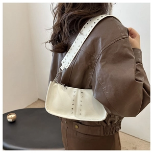 Détail d'un sac bandoulière en cuir blanc avec rivets argentés et large sangle à œillets