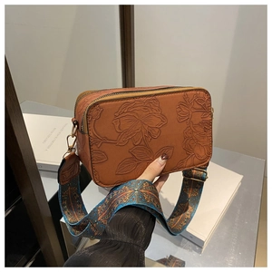 Detail of vintage brown camera bag featuring 3D rose embossing and colorful woven strap