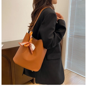 Brown lychee leather bucket bag with silk scarf detail worn by model in casual setting