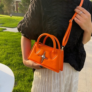 Orange mini square bag with silver star ornament and adjustable strap in outdoor scene