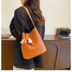 Detail of caramel leather bucket bag featuring a silk scarf and textured litchi grain