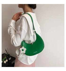 Detail of green crescent shoulder bag with silver logo and white flower charm on model