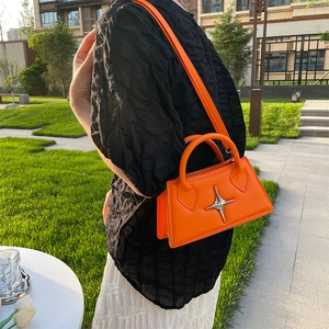 Outdoor shot of an orange crossbody bag with a silver star charm on a lush green lawn