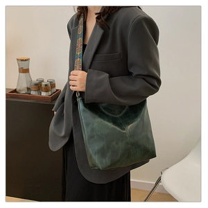 Detail of dark green textured leather tote bag with wide ethnic embroidered shoulder strap