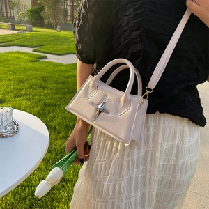 White minimalist square crossbody bag with star-shaped buckle shown in an outdoor setting