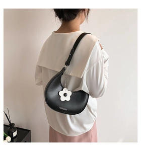 Detail view of the black half-moon shoulder bag with a white flower charm on the model