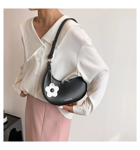 Detail of matte black crescent bag featuring silver zipper and white floral accessory
