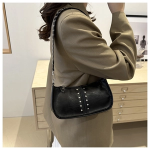 Détail du sac en similicuir noir avec rivets argentés porté sur un blazer kaki