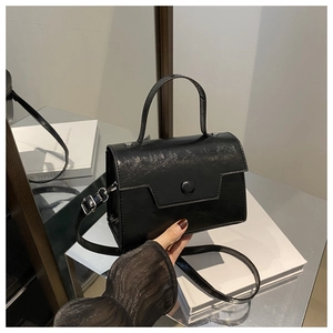 Dettaglio borsa a tracolla nera semi-opaca con patta sagomata e chiusura magnetica tonda