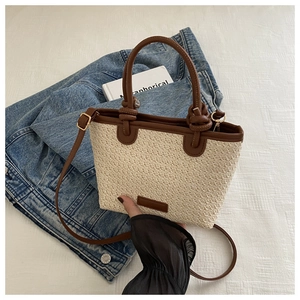 Détail du sac en paille tressée avec lanières en cuir marron foncé et bandoulière réglable