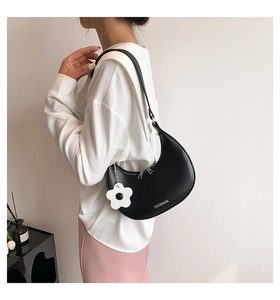 Detail of black crescent shoulder bag with white flower charm and adjustable metal buckle