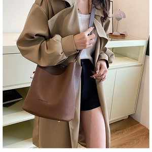Sac seau en cuir marron avec texture litchi et bandoulière porté par un mannequin