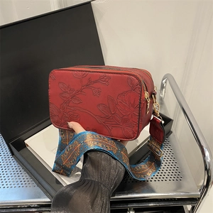 Red crossbody bag with floral embossing and colorful woven wide strap on black gift box