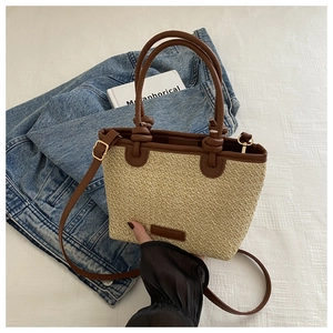 Détail d'un sac cabas en paille avec poignées en cuir marron tenu à la main