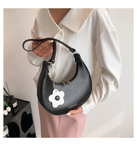 Detail of black crescent handbag with white flower charm and silver zipper closure