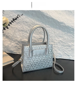 Detail of silver handbag with geometric rhombic texture and round handles on a pedestal