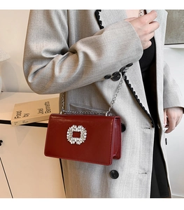 Détail d'un sac bandoulière en cuir rouge foncé avec boucle en cristal et bandoulière chaîne