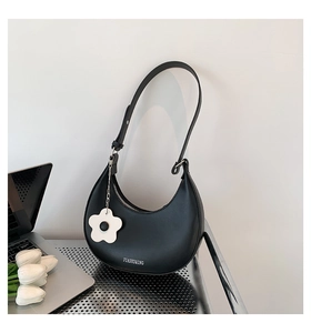 Detail of black crescent shoulder bag with silver hardware and white floral pendant