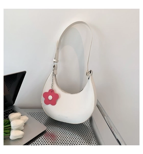 Detail of white crescent shoulder bag with pink floral charm against a clean wall