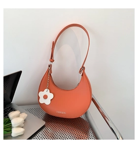 Detail of orange crescent hobo bag with floral charm on a desk with a laptop