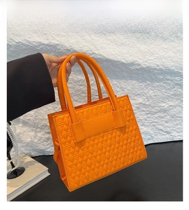 Close-up of bright orange quilted leather handbag featuring a modern rectangular structure
