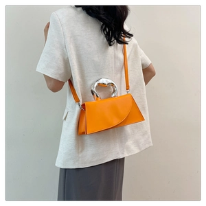 Detail of minimalist orange crossbody bag featuring fluid silver metal handle and leather strap