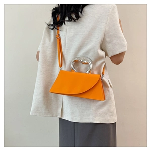 Minimalist bright orange crossbody bag with unique silver handle shown on white blazer