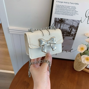 Mini sac bandoulière blanc avec nœud argenté et chaîne en métal dans un décor de vie