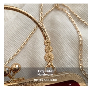 Macro detail of red velvet handbag featuring golden floral metal handle and vintage carving
