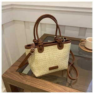 Détail du sac en paille tressée avec poignées en cuir marron et bandoulière réglable
