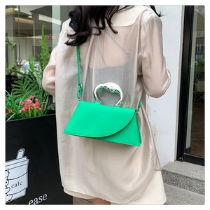 Green square bag detail with silver wavy handle shown on model in a casual street setting
