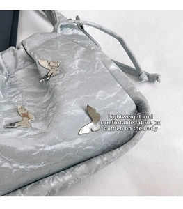 Dettaglio della borsa a secchiello argento metallizzato con texture plissettata e fiocchi
