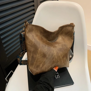 Vintage brown leather tote bag with a wide ethnic patterned strap on a white chair