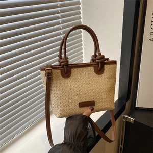 Minimalist beige woven straw tote bag with brown leather handles and adjustable strap