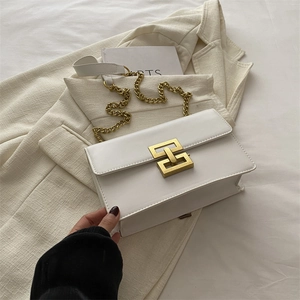 Minimalist beige leather shoulder bag with gold chain strap on a cream blazer
