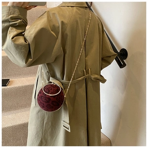 Detail view of burgundy leopard print round crossbody bag with gold chain on model
