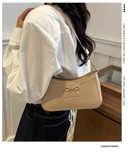 Detail of beige hobo shoulder bag with a gold metal bow and fine stitching accents