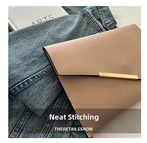 Detail of light beige envelope bag with golden bar on denim and arts book