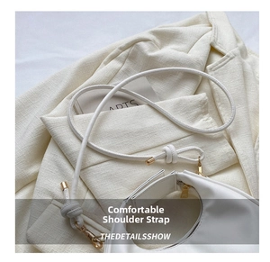 Detail of white half-moon bag featuring knotted shoulder strap and gold hardware