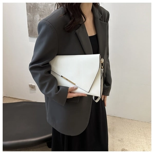 Detailed view of white envelope clutch bag with gold metal trim held by a fashion model