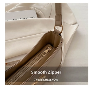 Close-up of smooth gold zipper and hardware on a beige PU leather baguette shoulder bag