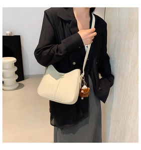 Chic beige crescent shoulder bag with metal tag and cute plush bear charm on a model