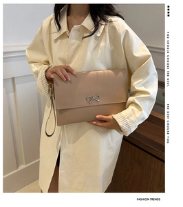 Detail of elegant beige envelope clutch featuring a decorative silver metal bow