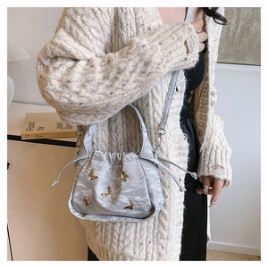 Détail du sac seau gris avec imprimé paysage et breloques papillons dorés sur le mannequin