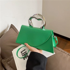 Minimalist green trapezoid handbag with a sculptural silver metal handle and shoulder strap
